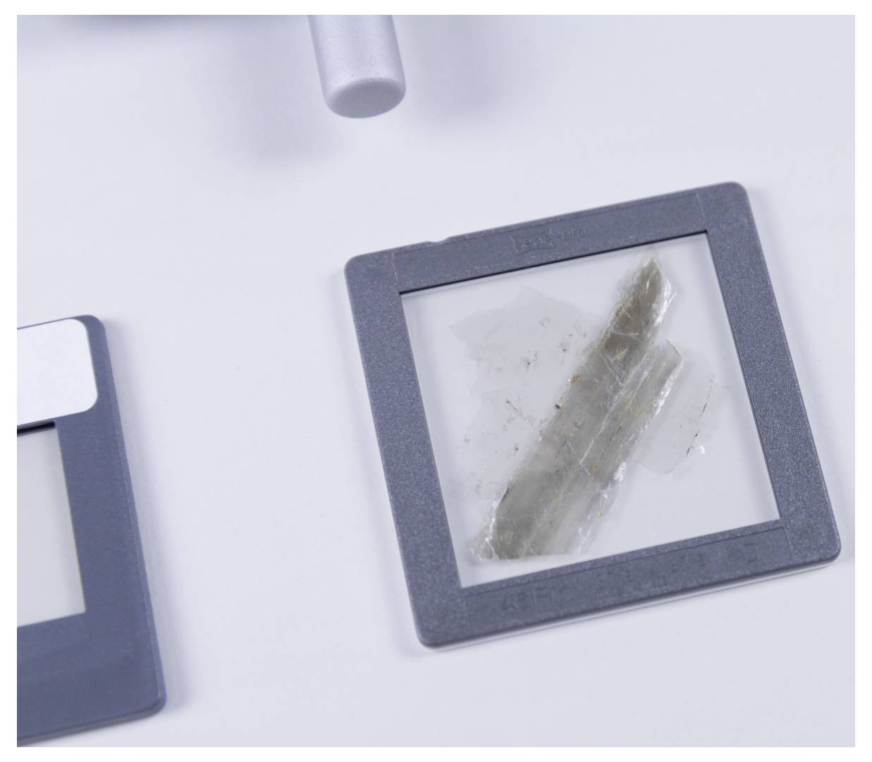 A close-up of a microscope slide showing a thin, transparent specimen under examination. Surrounding slides are partially visible.