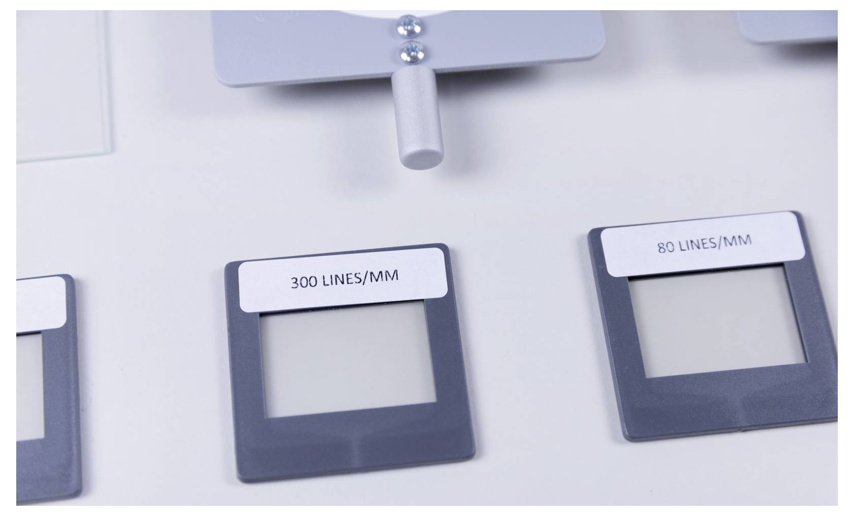 A close-up of three square frames labeled '300 LINES/MM' and '80 LINES/MM'. Two frames have empty centers; one has a rod attached above.