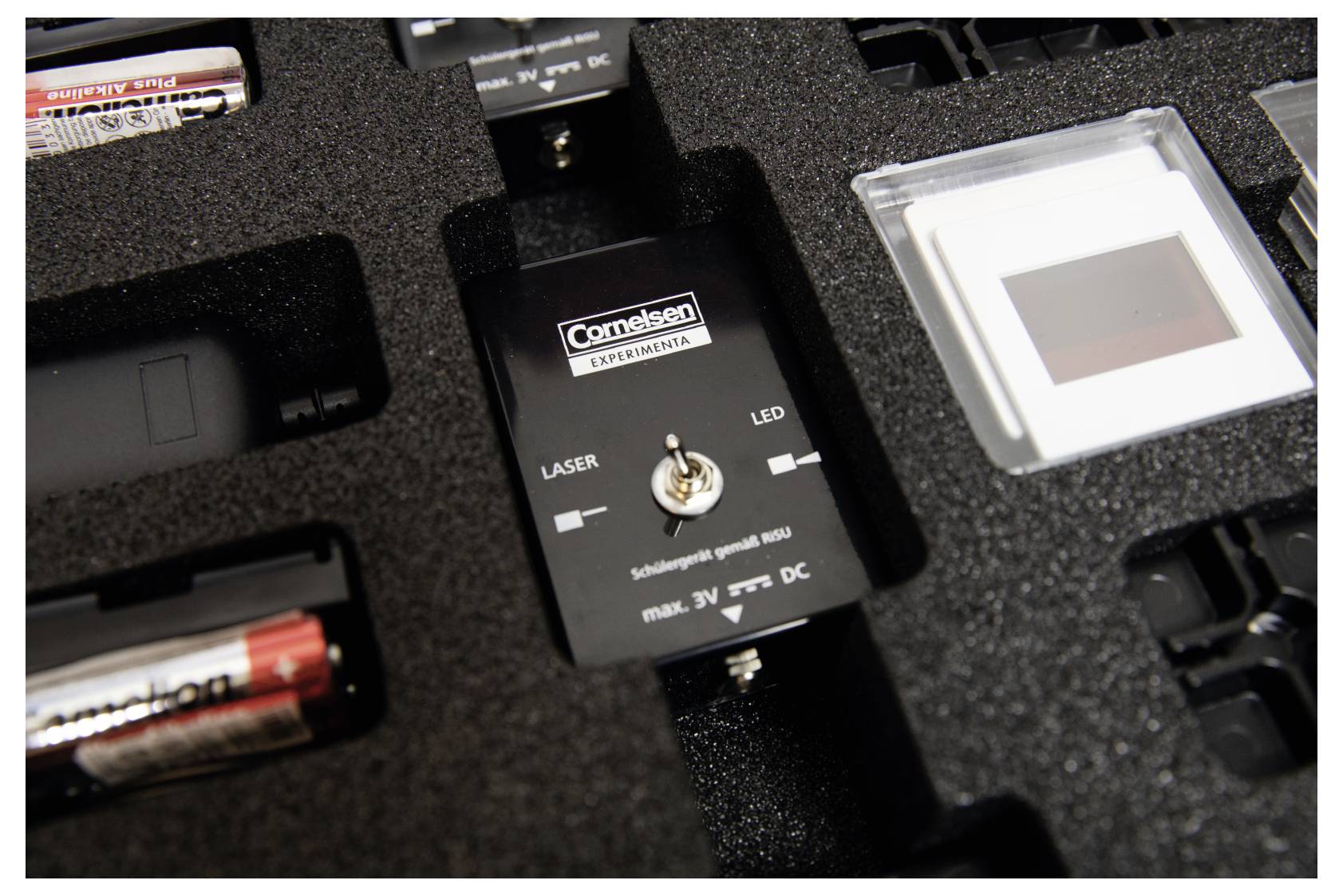 A close-up of a foam case containing a device labeled 'Comteleon Experiments' with a toggle switch marked 'Laser' and 'LED'.