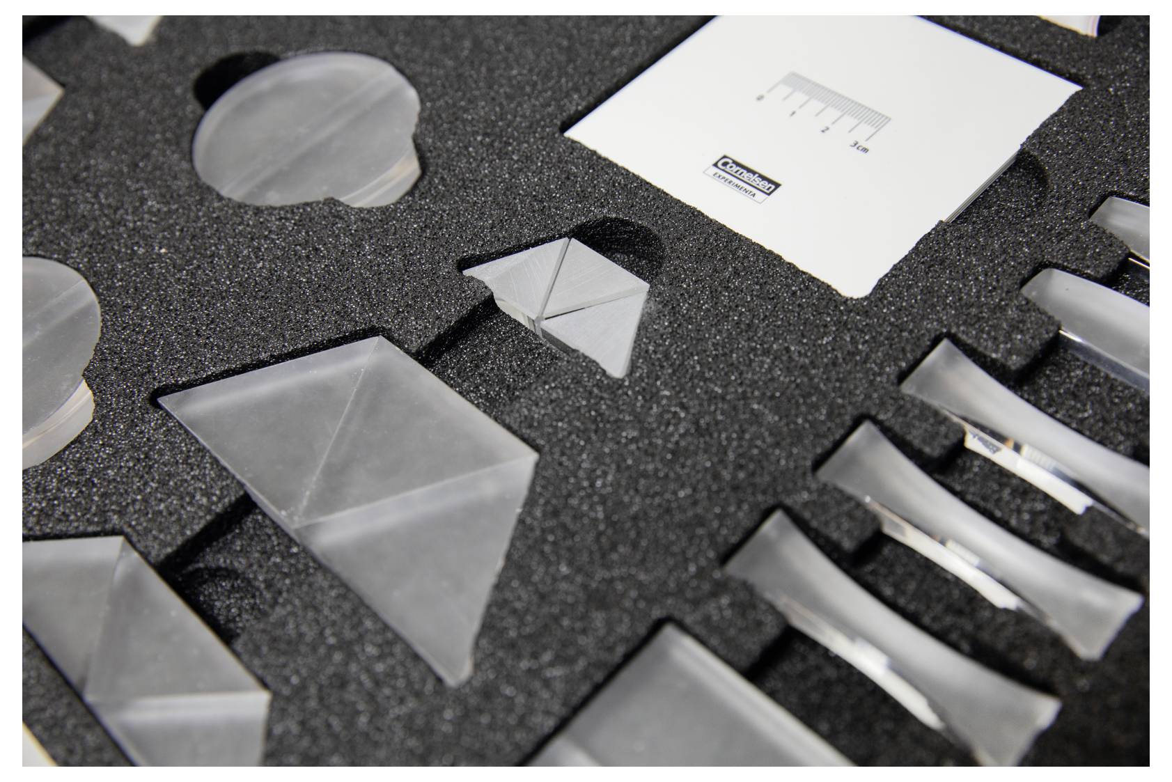 Foam insert with various slots holding plastic geometric shapes, including triangles and rectangles, alongside a measurement card.