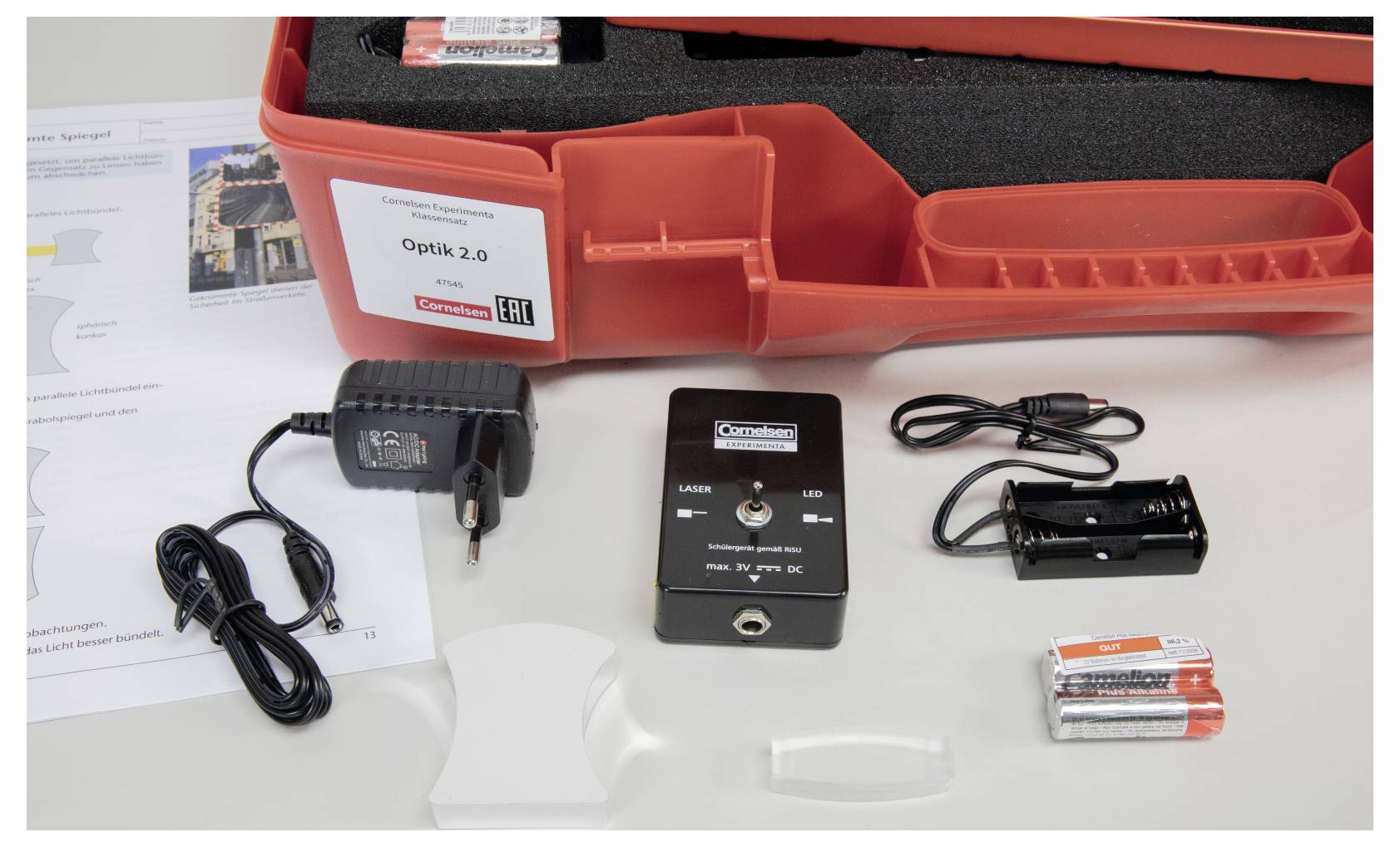 Image of a science lab kit labeled 'Optik 2.0' including a power adapter, battery holder, batteries, and additional components inside a red case.