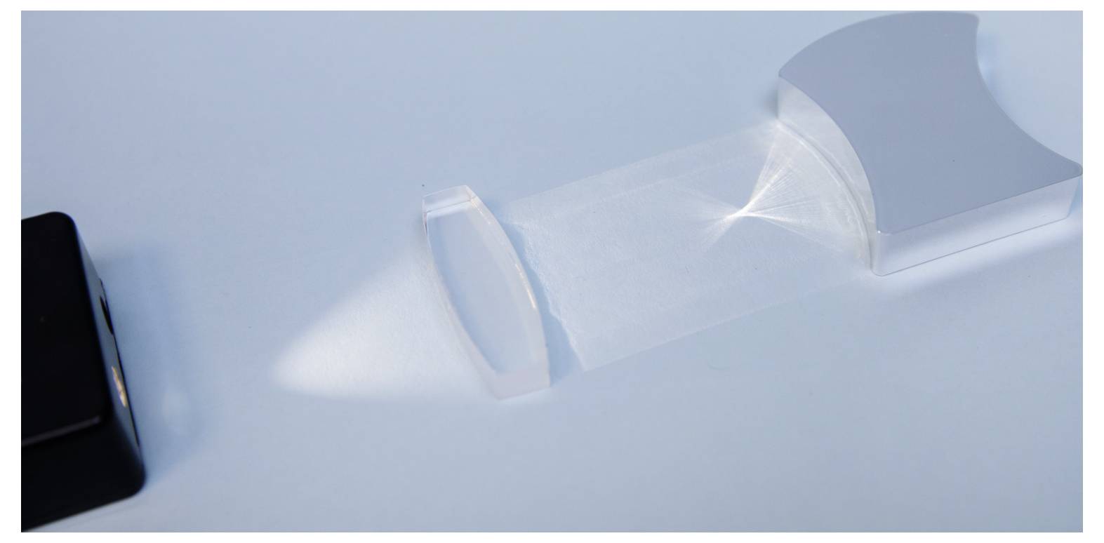 A beam of light passes through a transparent prism, creating a focused projection on a flat surface, demonstrating light refraction.
