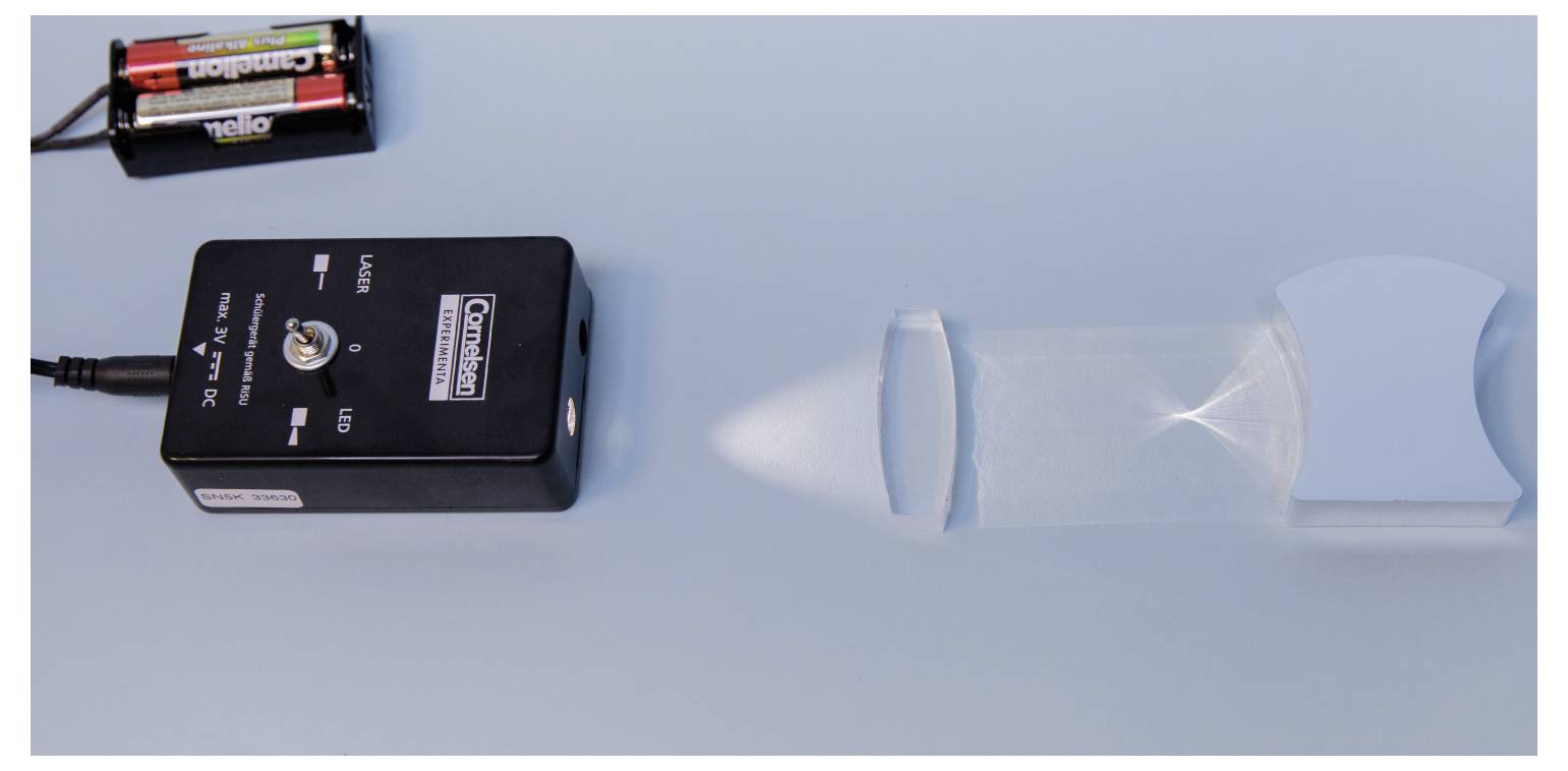 'A black laser module projects a light beam towards a concave mirror on a blue surface, demonstrating light reflection principles.'