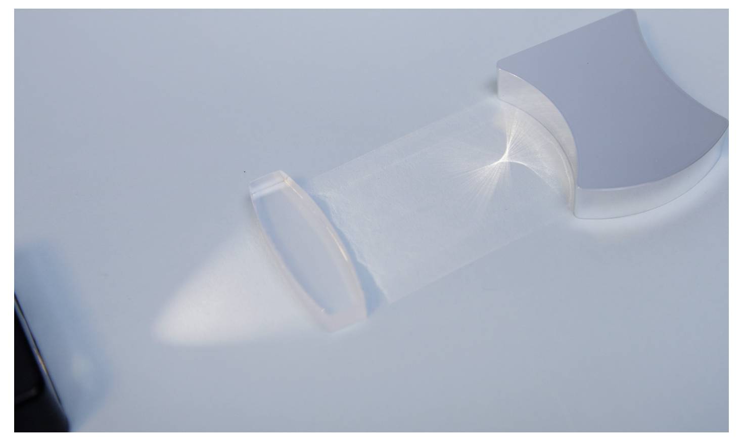 A transparent block on a white surface refracts light, creating a focused beam.