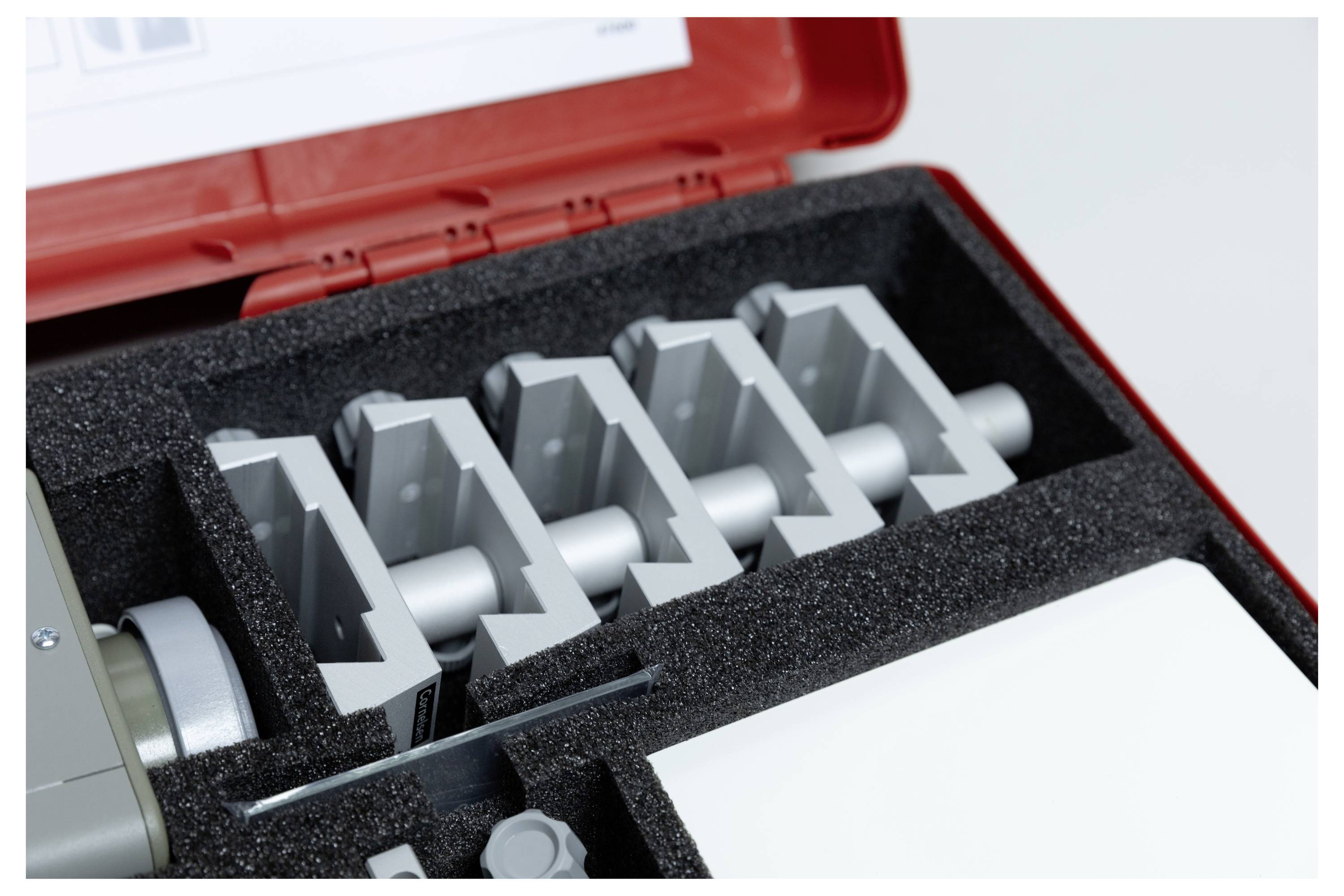 'A red case with protective foam holding gray metal blocks arranged in a row. The top of the case has a white label with text.'