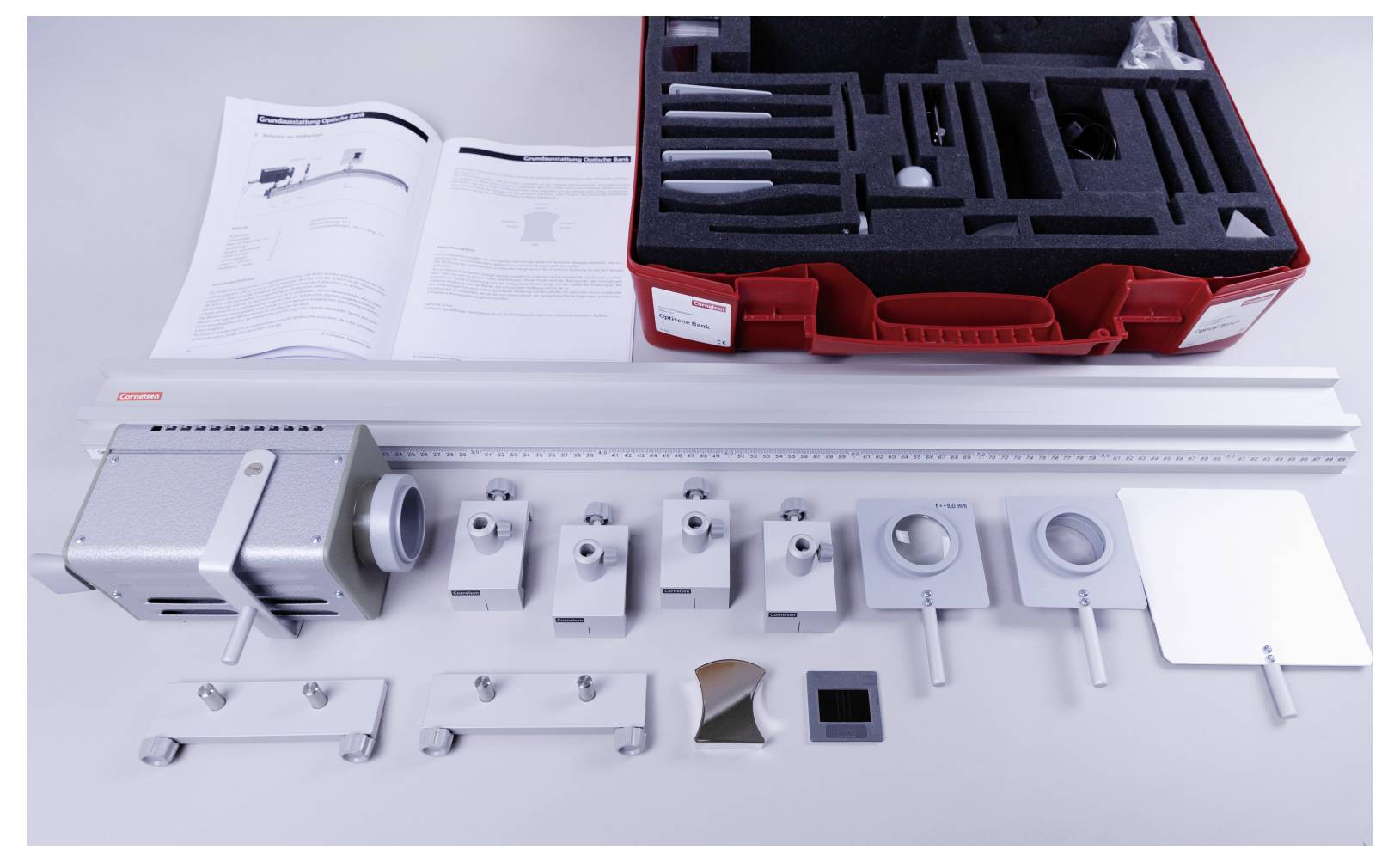 A red toolkit box with various metal components, instruction manuals, and measuring devices arranged on a table, suggesting assembly or setup.