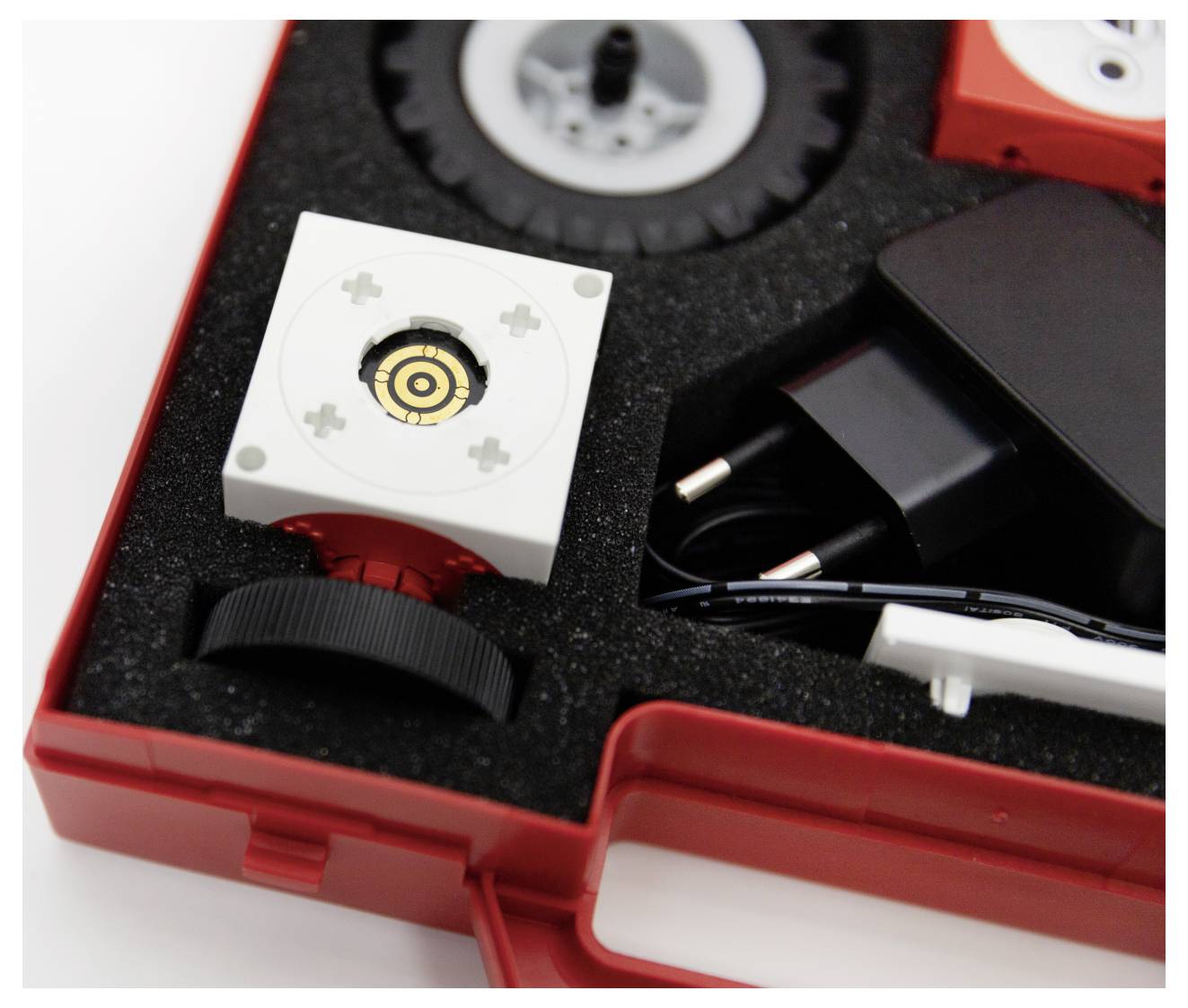 A red case containing a camera lens, wheel, and cables, organized in foam compartments.