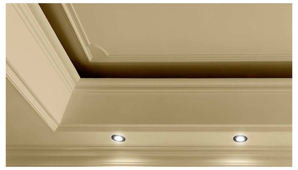 A beige ceiling with decorative molding and two recessed lights illuminating a room.