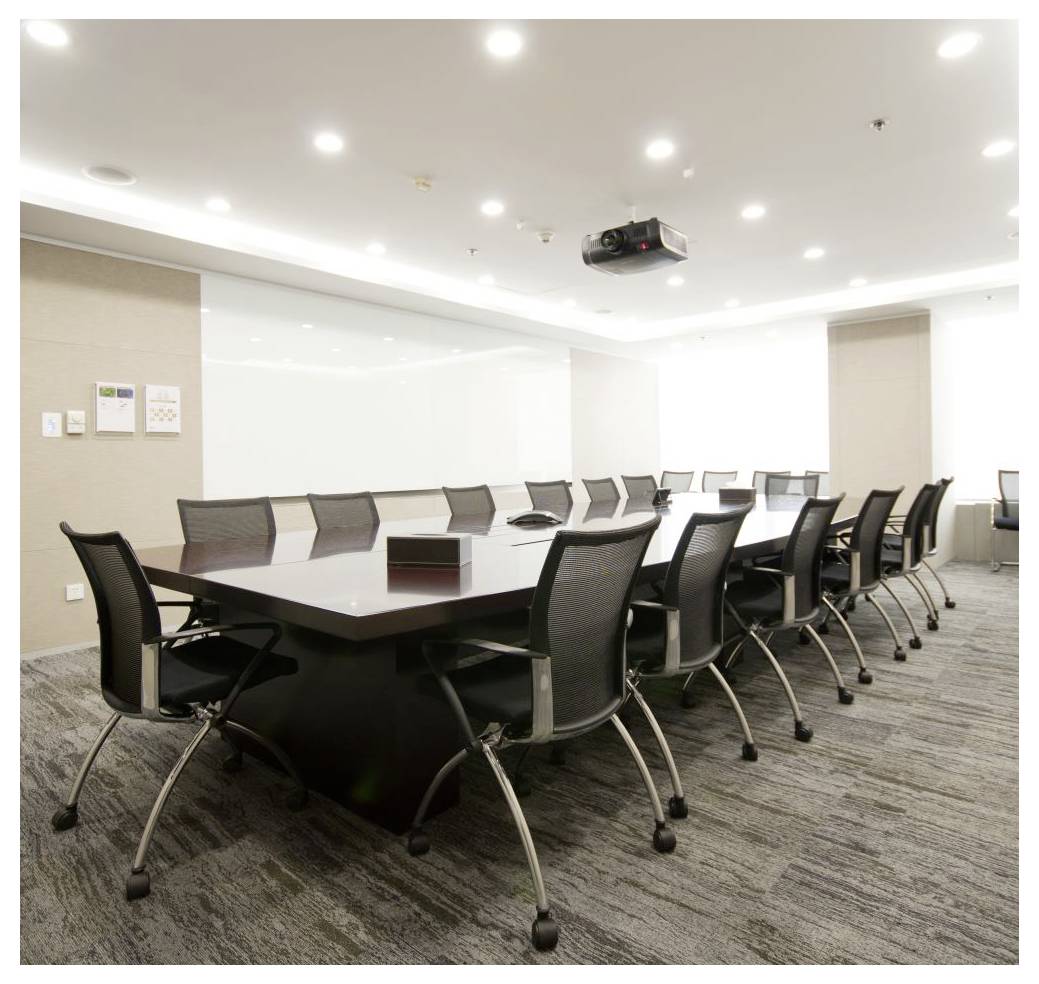 A spacious, well-lit conference room with a long, rectangular table surrounded by modern office chairs under ceiling lights.
