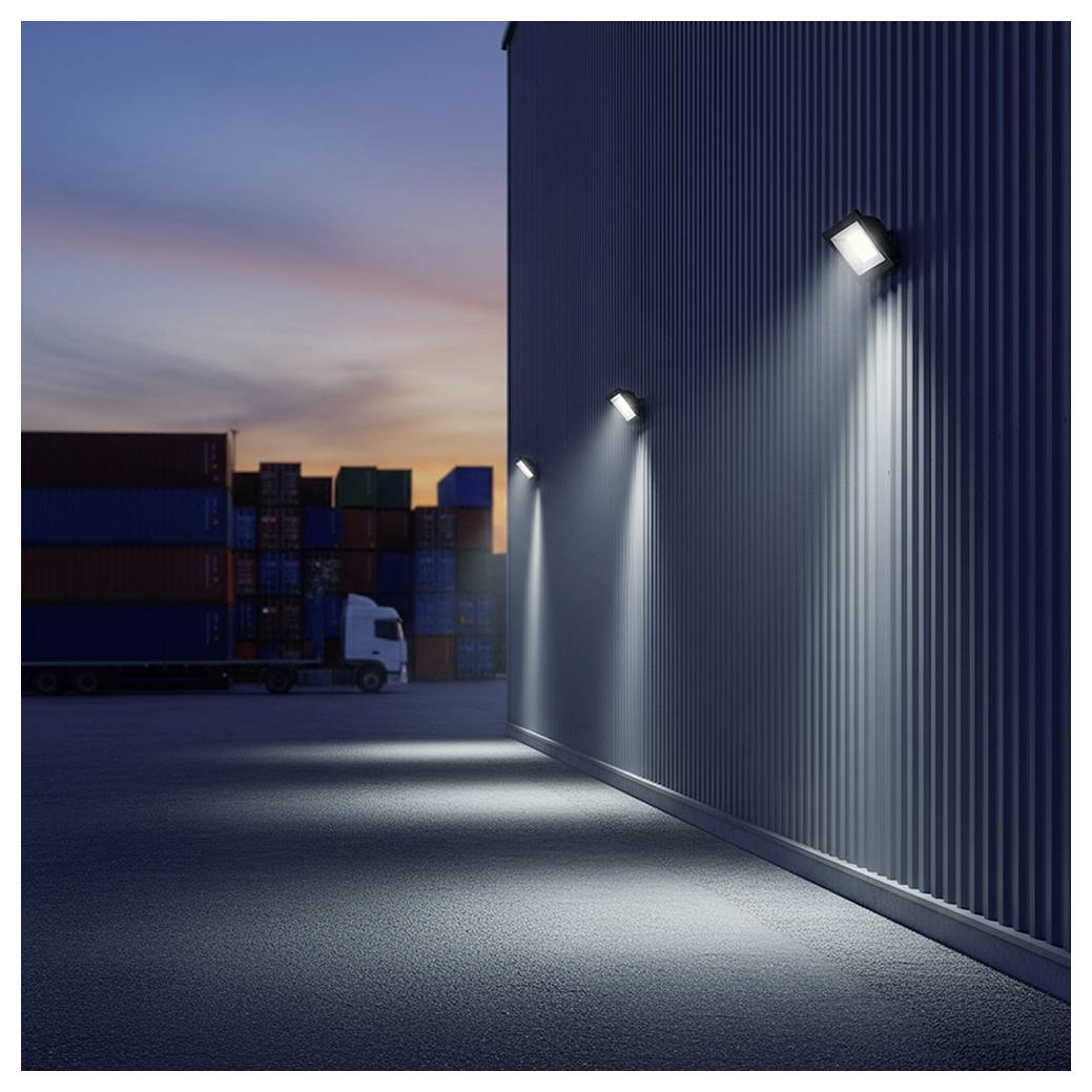 A dimly lit industrial area at dusk with shipping containers and a parked truck. Wall-mounted lights illuminate a corrugated metal wall.