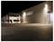 A large industrial building illuminated at night, showcasing modern architecture with metal siding and a wide paved area in the foreground.