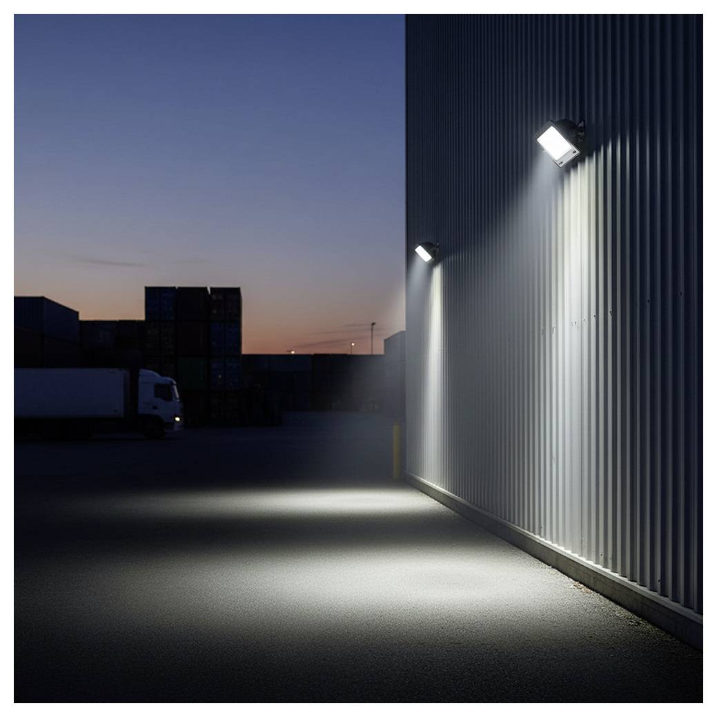 A dimly lit industrial area at dusk, showing a truck, stacked shipping containers, and bright lights illuminating a corrugated metal wall.