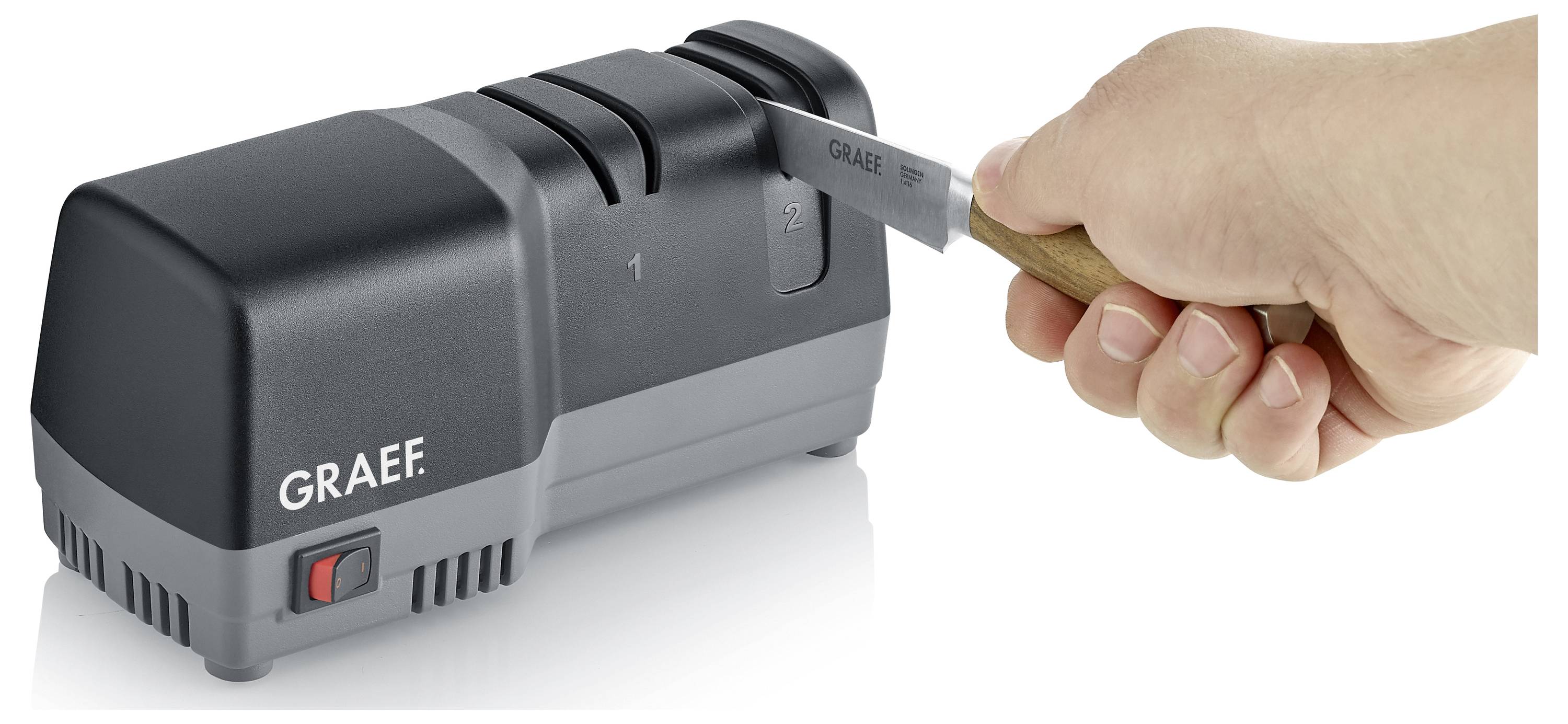 A person sharpens a knife with an electric sharpener labeled 'Graef', focusing on the sharpening grooves numbered '1' and '2'.