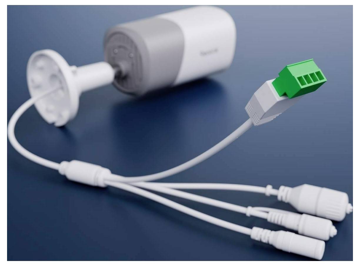 A security camera with multiple connectors, including a green terminal block plug, is situated on a blue surface.