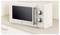 A beige microwave oven with two dials for settings sits on a light-colored kitchen counter against a tiled backsplash.