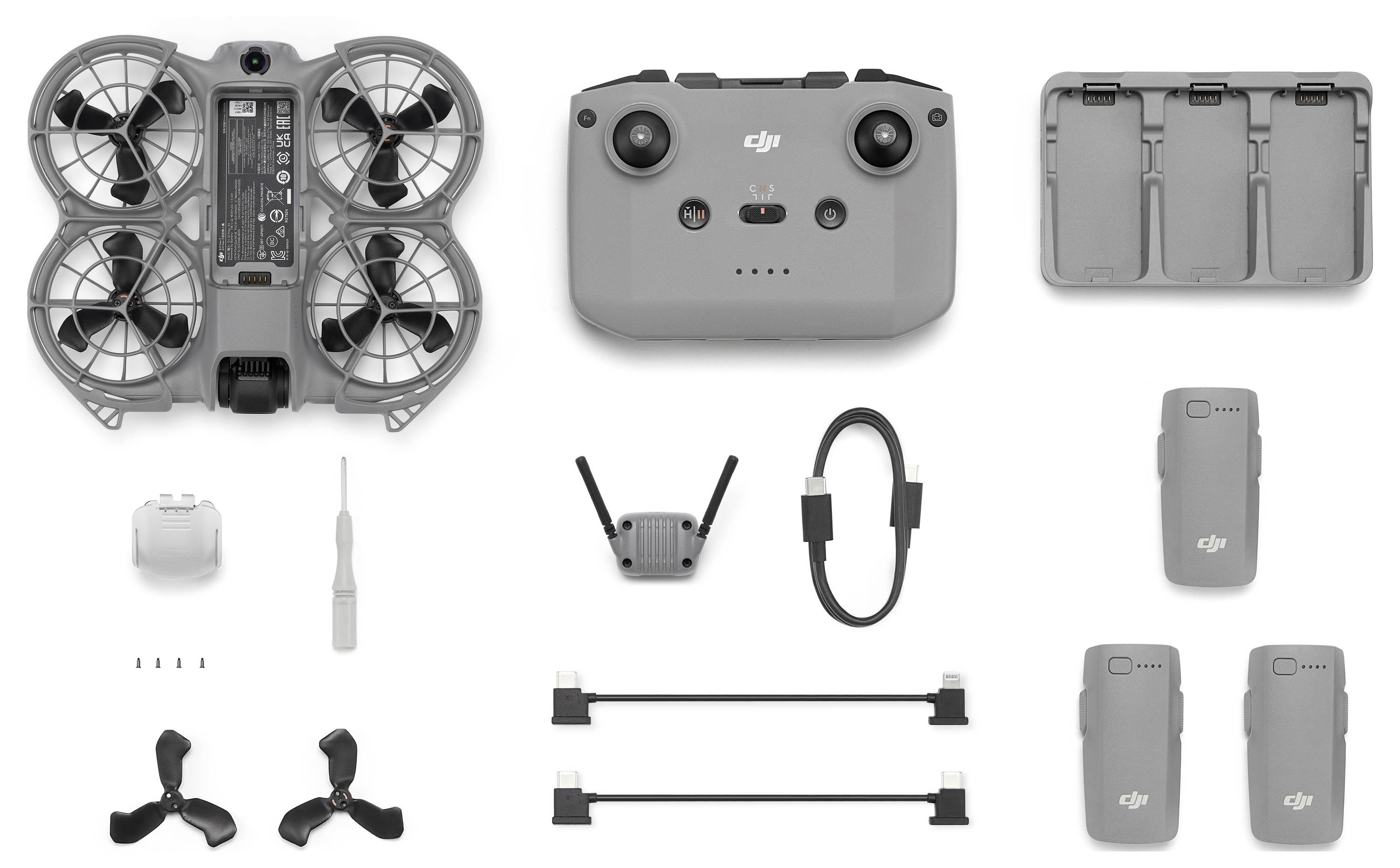A compact drone kit featuring a small drone, remote control, two batteries, propellers, a charging hub, and connectors on a white background.