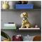 A LEGO model of a Labrador puppy sits on a shelf, holding a pink toy. Surrounding items include books, a vase, and decorative objects.