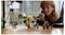 A child focuses on assembling a detailed spaceship model with small character figurines, on a wooden table, in a bright room.