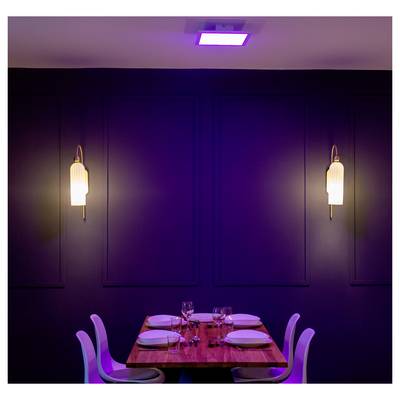 A dimly lit dining room with a wooden table set for four, featuring white chairs, plates, glasses, and two wall lamps against a dark background.