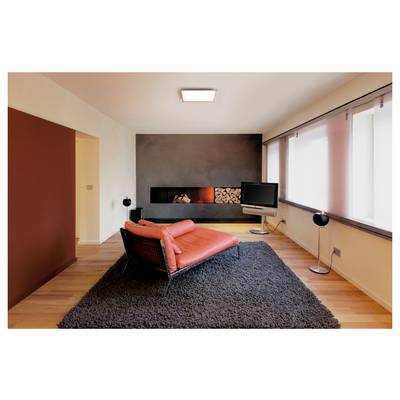 A modern living room with a red lounge chair on a dark rug, facing a TV. A built-in fireplace with stacked logs is on the left wall.