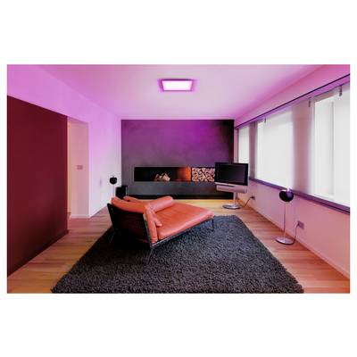 A modern living room with a red chaise lounge, black rug, wall-mounted TV, and fireplace. The room is illuminated with pink lighting.