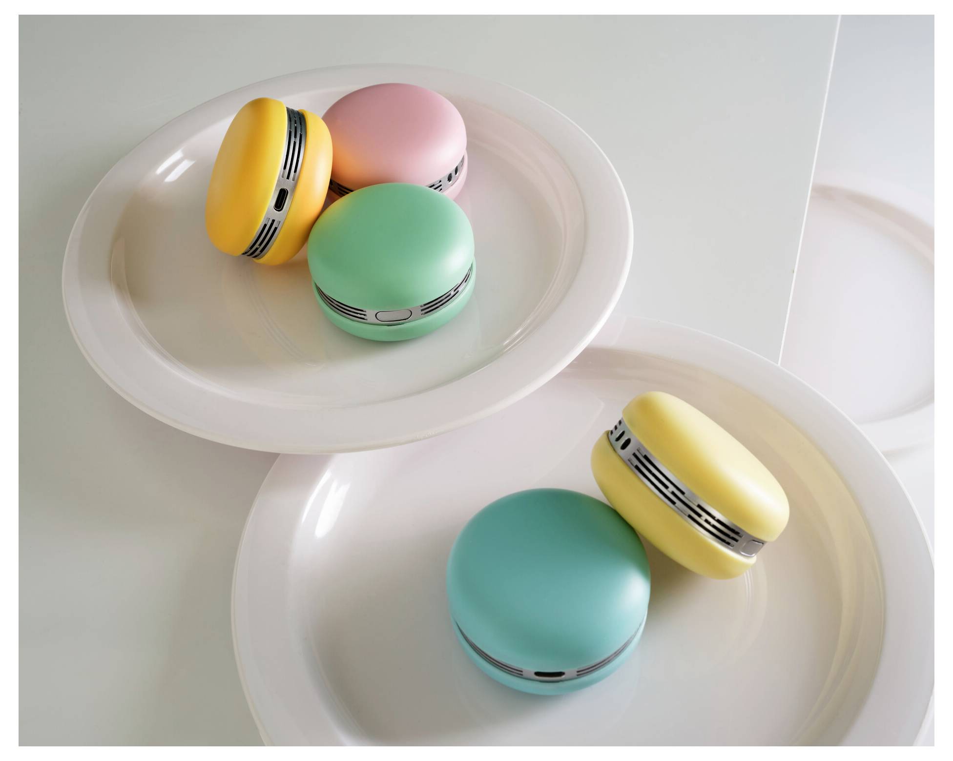 Three colorful macaron-shaped objects, yellow, pink, and teal, on a reflective white surface.