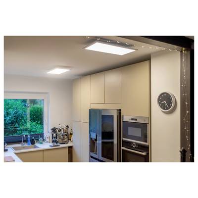 A modern kitchen with beige cabinets, a blue fridge, and built-in appliances. A wall clock shows 12:15. A window reveals greenery outside.