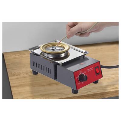 'A hand holding a wire is dipping it into a small electric solder pot on a wooden table. The pot is set to 200 degrees Celsius.'