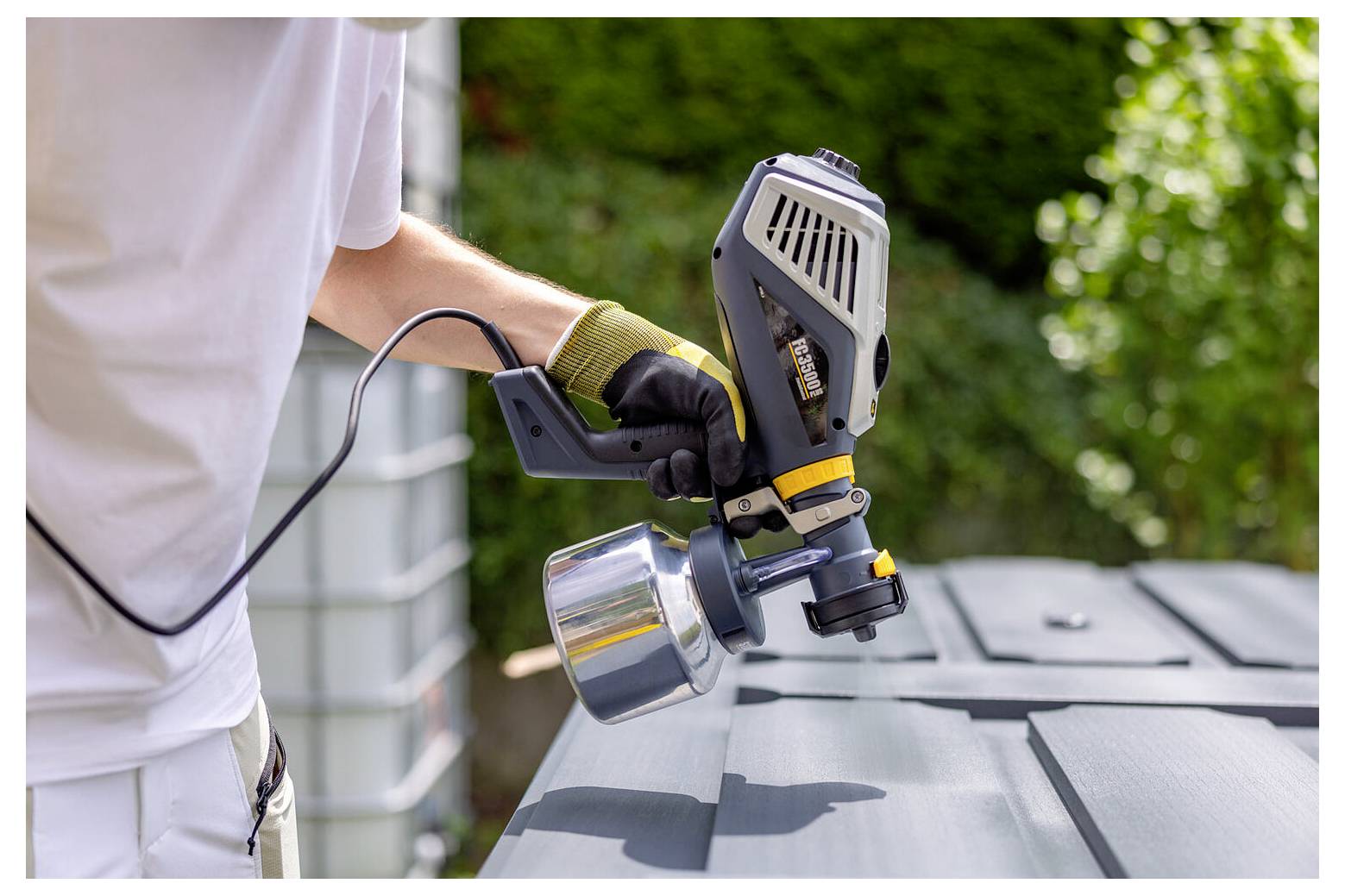 'A person using a paint sprayer to apply paint on a metal surface outdoors, wearing gloves for protection.'
