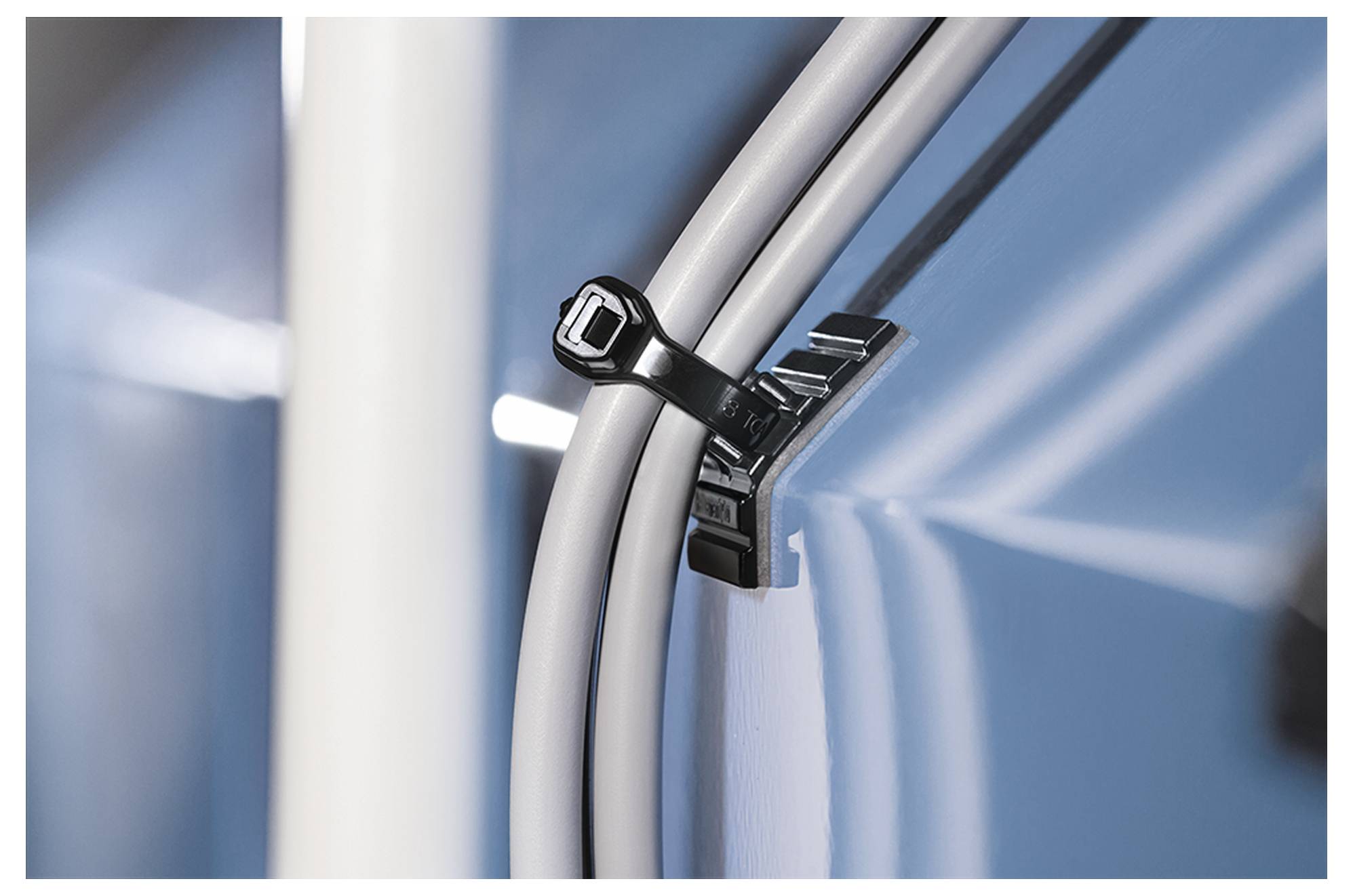 A black cable tie secures two white cables to a glossy blue surface, with a close-up view highlighting the tie's locking mechanism.