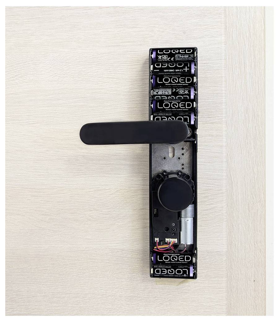 A wooden door displays a partially disassembled black electronic lock, showing internal components like wiring and batteries.