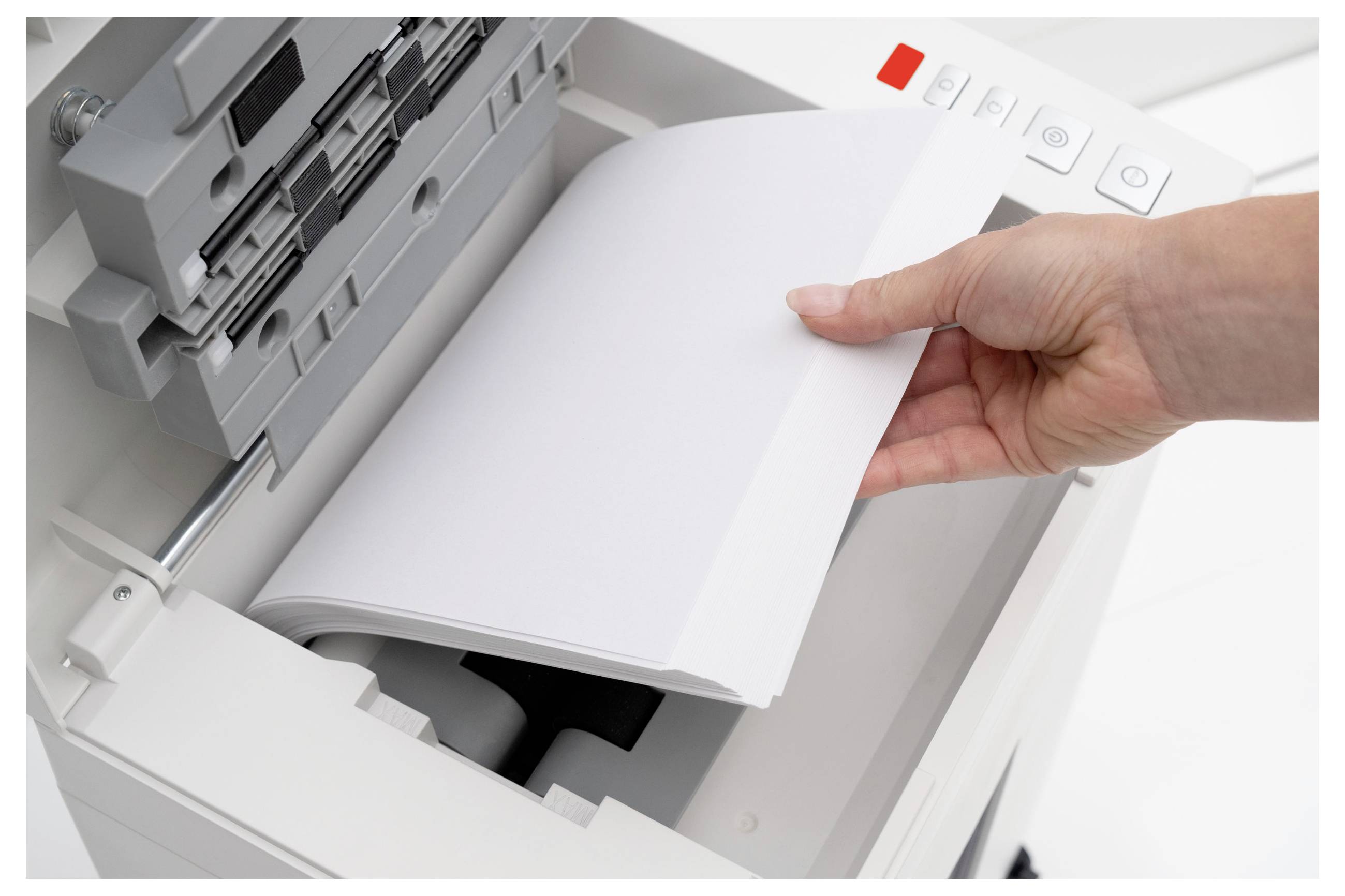 A hand places paper into a copier machine's tray, preparing for printing. The copier has control buttons visible on the side.