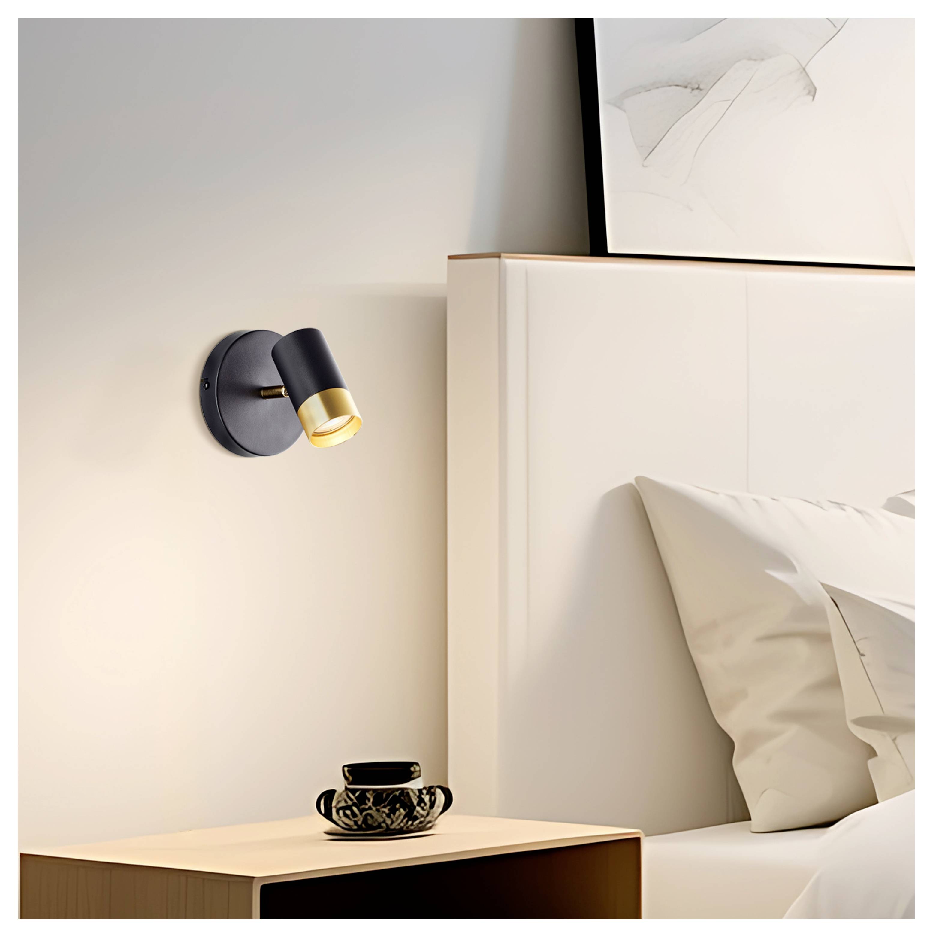 A modern wall-mounted lamp illuminates a bedside area with a wooden nightstand holding a black cup, next to a white bed and abstract art.