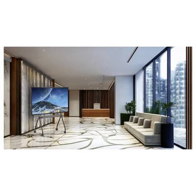 Modern office lobby with a large TV on a stand, reception desk, sofa seating, plants, and floor-to-ceiling windows overlooking city buildings.