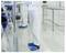 A person in a cleanroom suit and blue shoe covers operates equipment, suggesting a controlled laboratory environment.