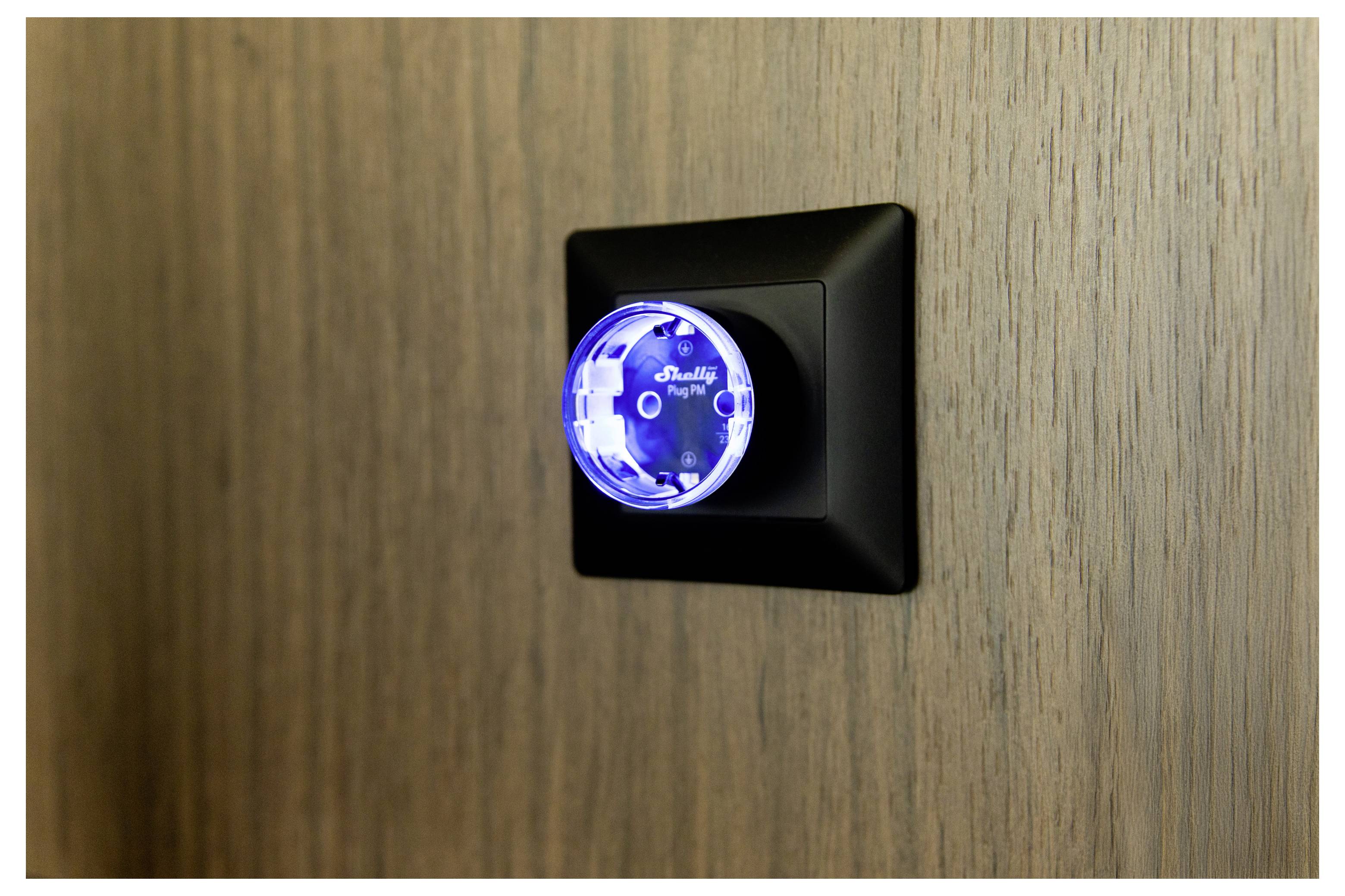 A black light switch with a glowing blue circular knob labeled 'BLUEFIN Night'. Mounted on a wooden wall.