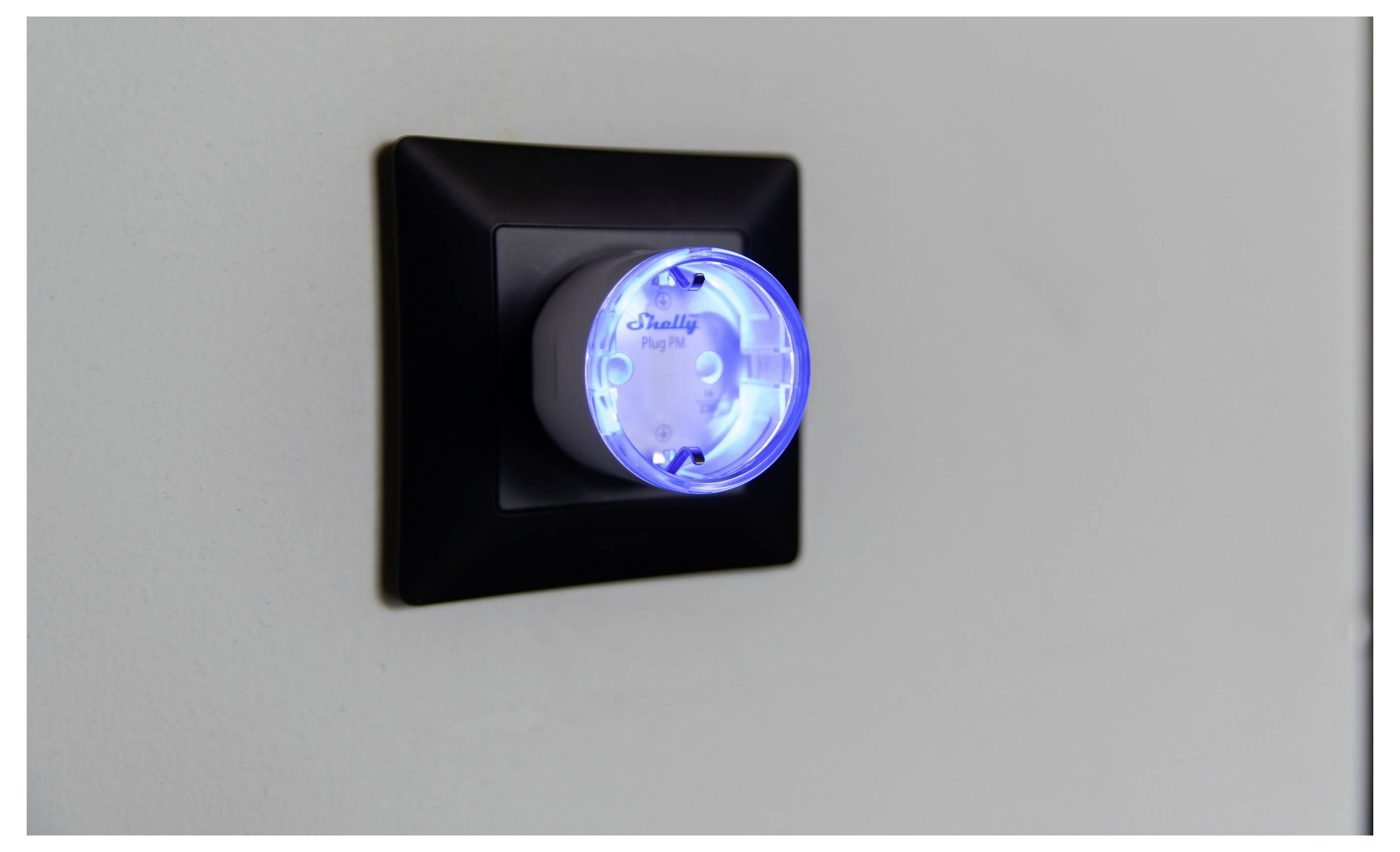 A wall outlet with a small, circular plug emitting a blue light, indicating power or connectivity status.