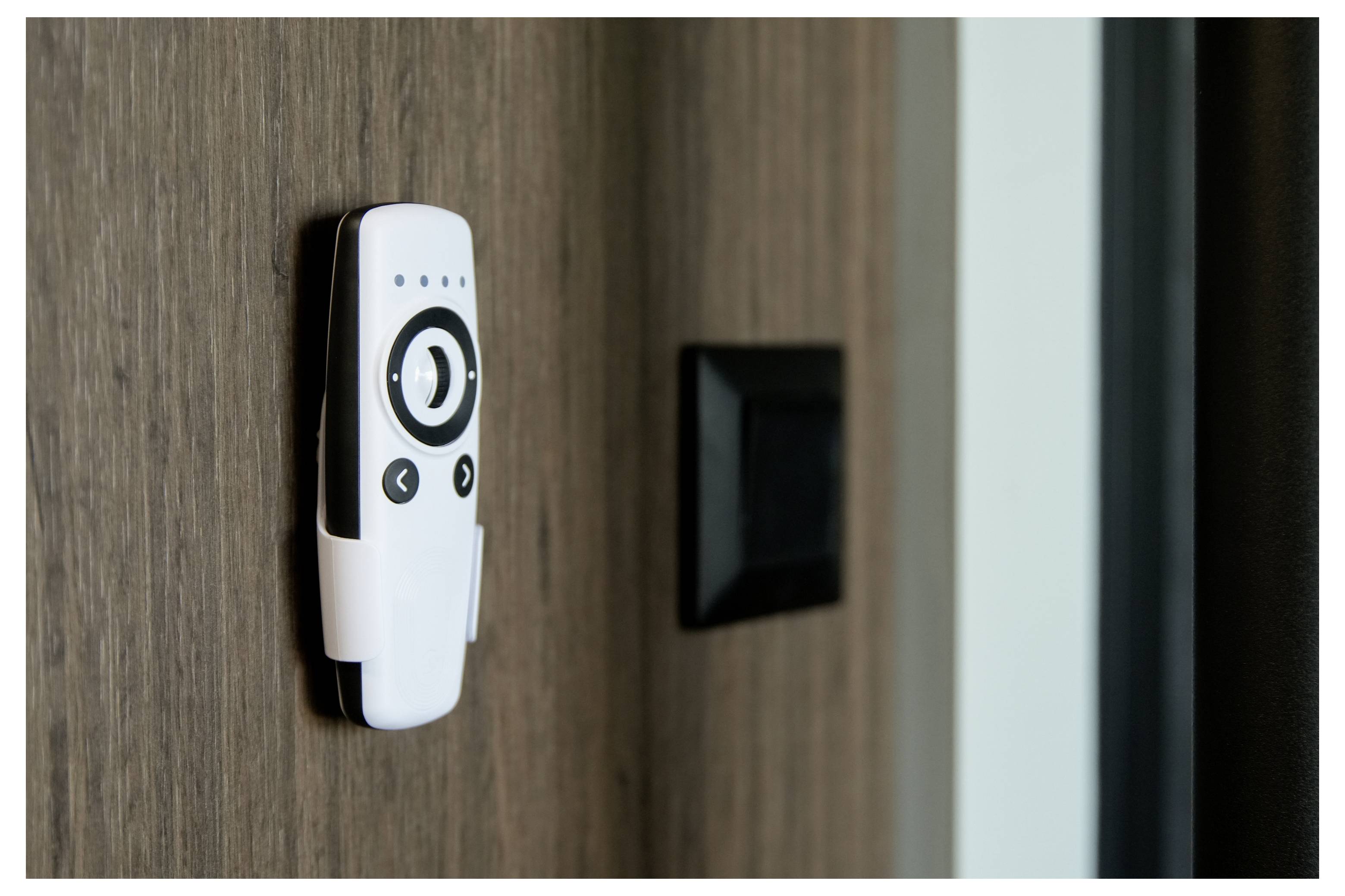 A remote control with buttons is mounted on a wooden wall beside a black switch, suggesting control of home devices or lighting.