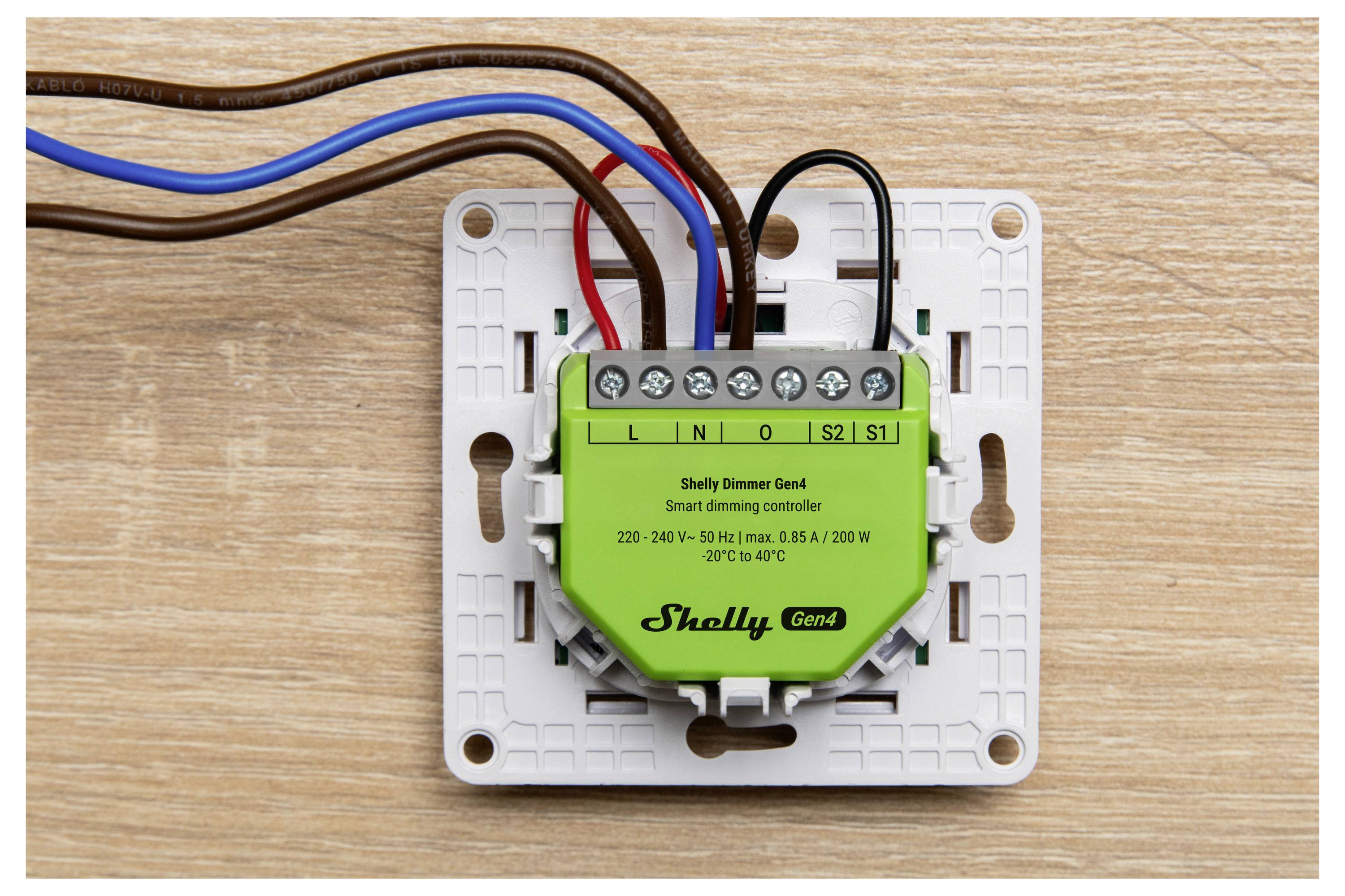 A green Shelly Dimmer 2 smart dimming controller with multiple wires connected, mounted on a wooden surface.