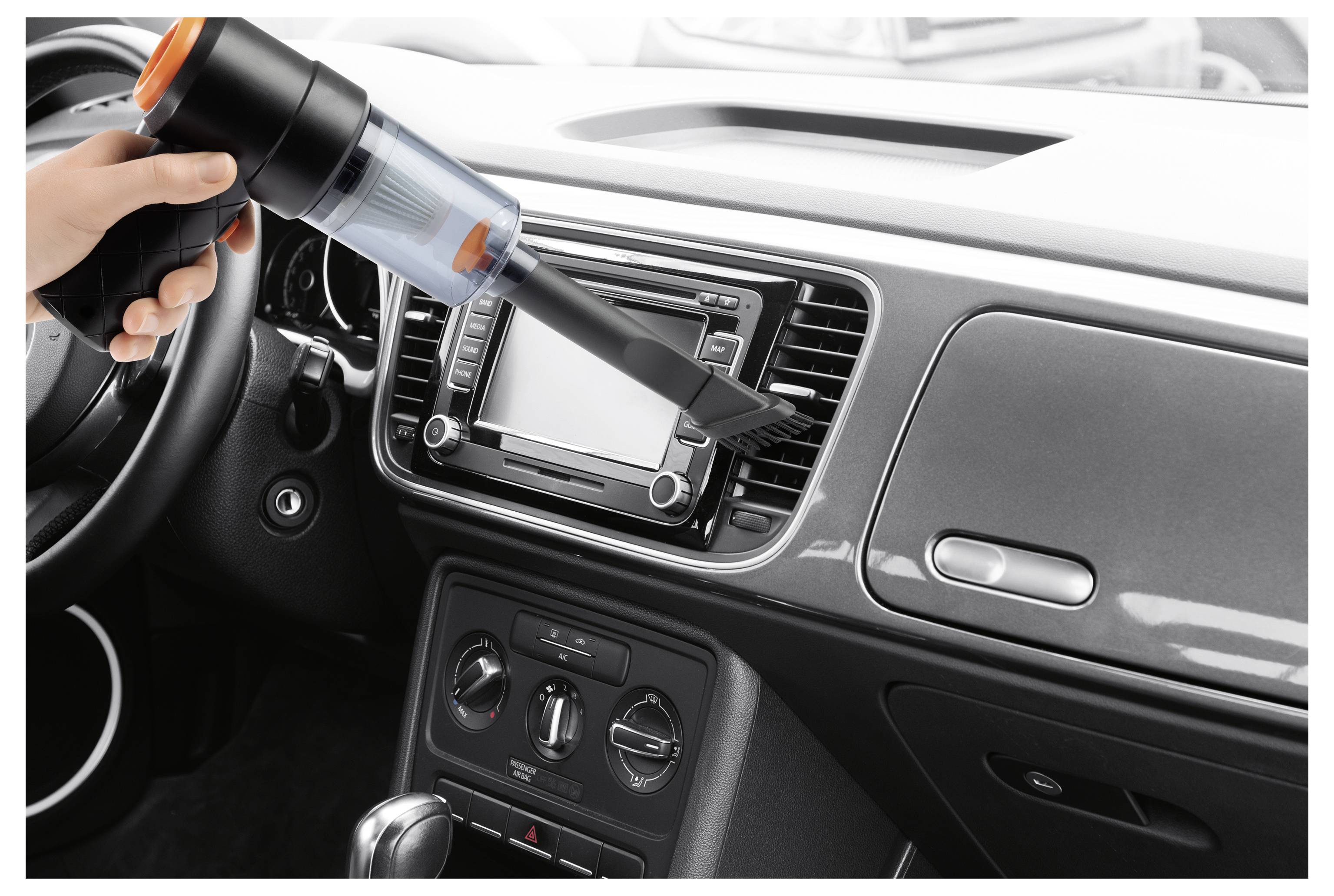 A person uses a handheld vacuum cleaner to clean the air vent of a car dashboard.