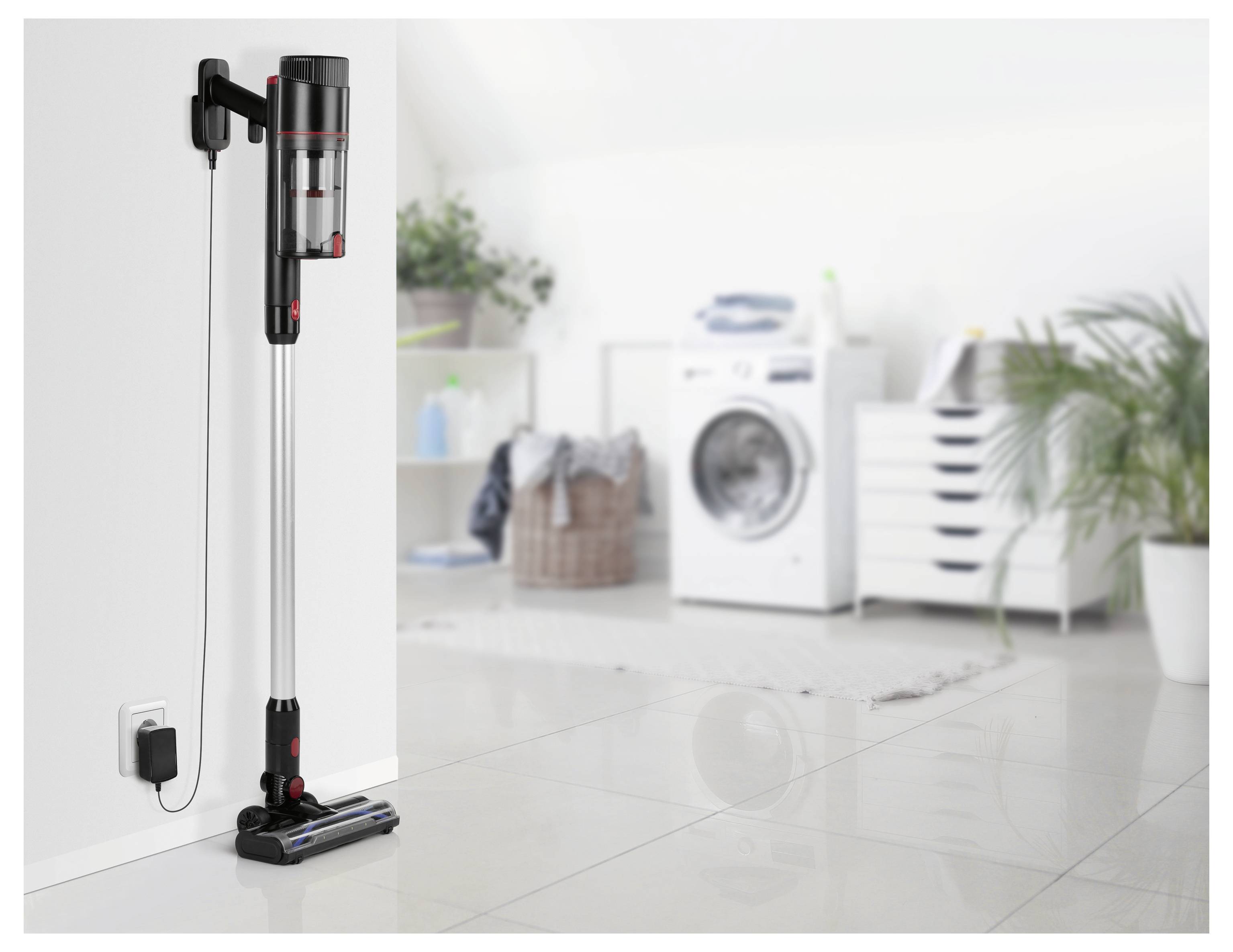 A cordless vacuum cleaner is mounted on a wall in a laundry room, near a washing machine and a basket.