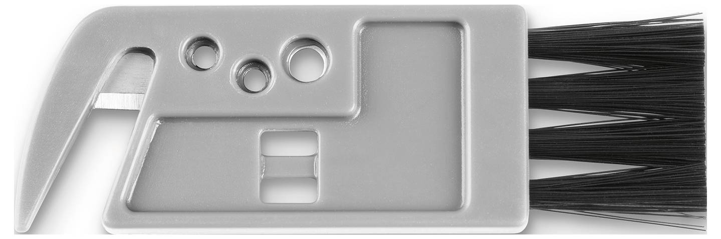 A gray multi-tool with a metal hook, holes for function, and bristles for cleaning, likely designed for computer keyboard maintenance.