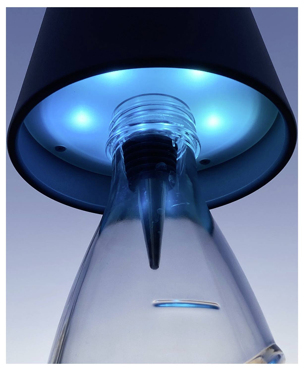 A close-up of a clear bottle illuminated by blue lights from a fixture above, creating a futuristic and aesthetic effect.