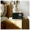 A digital radio displaying the time '3:12 PM' sits on a wooden nightstand, with decorative pottery and cotton stems.