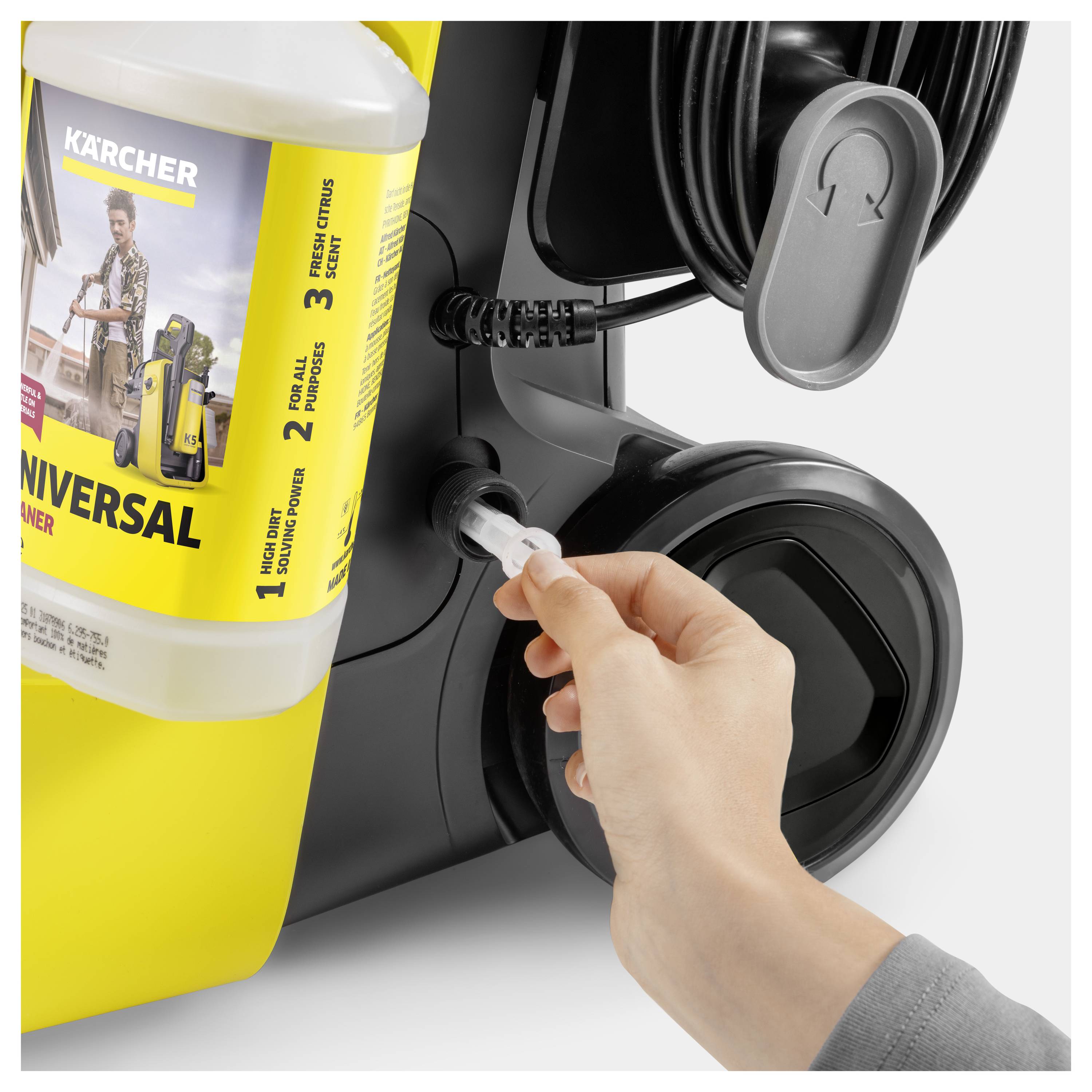 'Hand attaching a cleaning fluid bottle to a Kärcher pressure washer. The label shows instructions and universal cleaner text.'