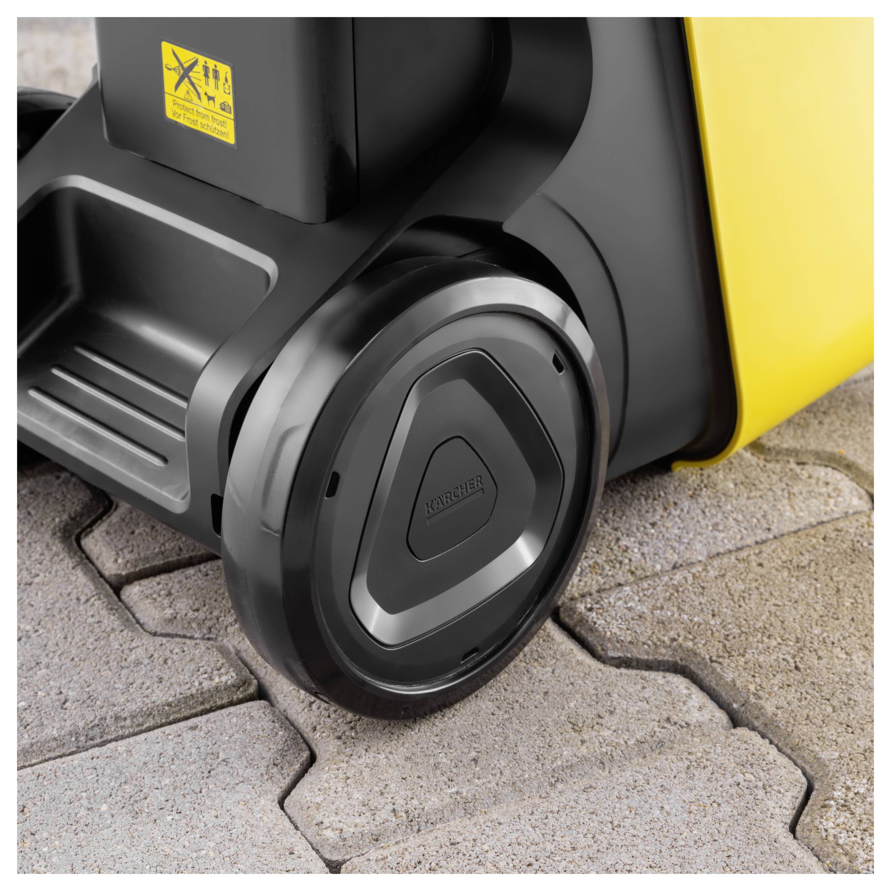 A close-up of a wheel on a yellow industrial cleaning machine on a cobblestone surface, highlighting the machine's sturdy design and texture.