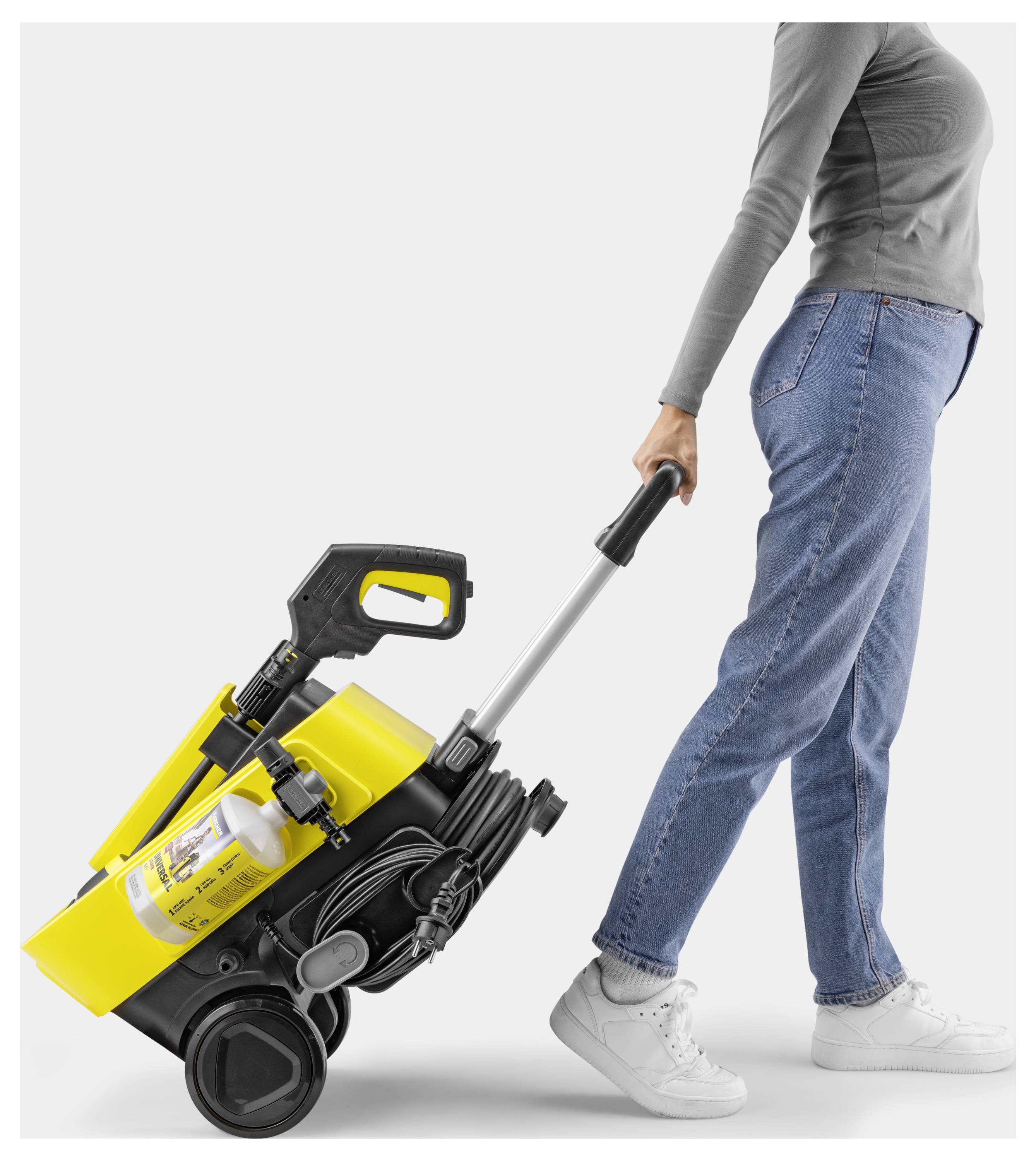 A person pulls a yellow and black portable cleaning device on wheels by its handle.