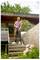 Man in casual clothing uses a pressure washer to clean the concrete steps outside a modern house surrounded by greenery and flowers.