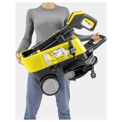 A person holding a yellow and black portable pressure washer with a built-in compartment for detergent bottles and a neatly coiled cable.