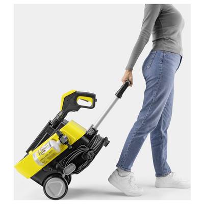 A person in jeans and a gray top pulls a yellow vacuum cleaner on wheels with a metal handle, highlighting its portability.